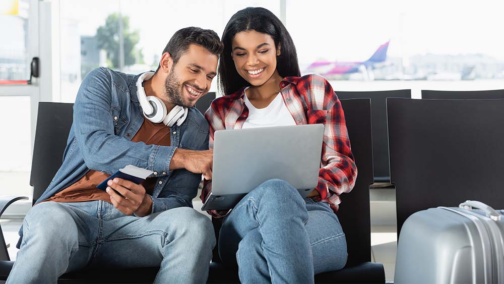 Happy young couple sitting in an airport looking at a laptop