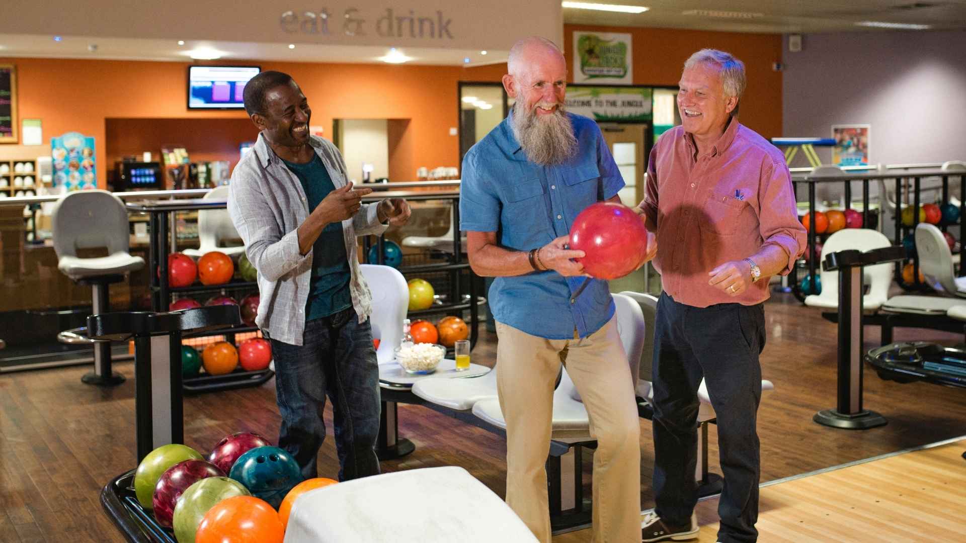 Mature male friends bowling together