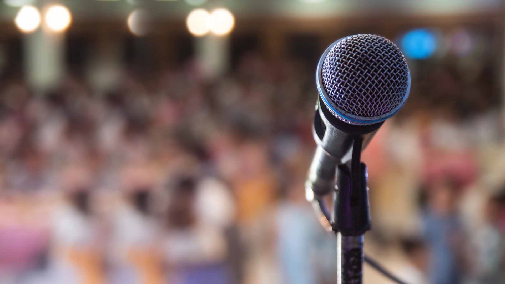 Microphone in stand in focus in front of a large group of meetings attendees out of focus