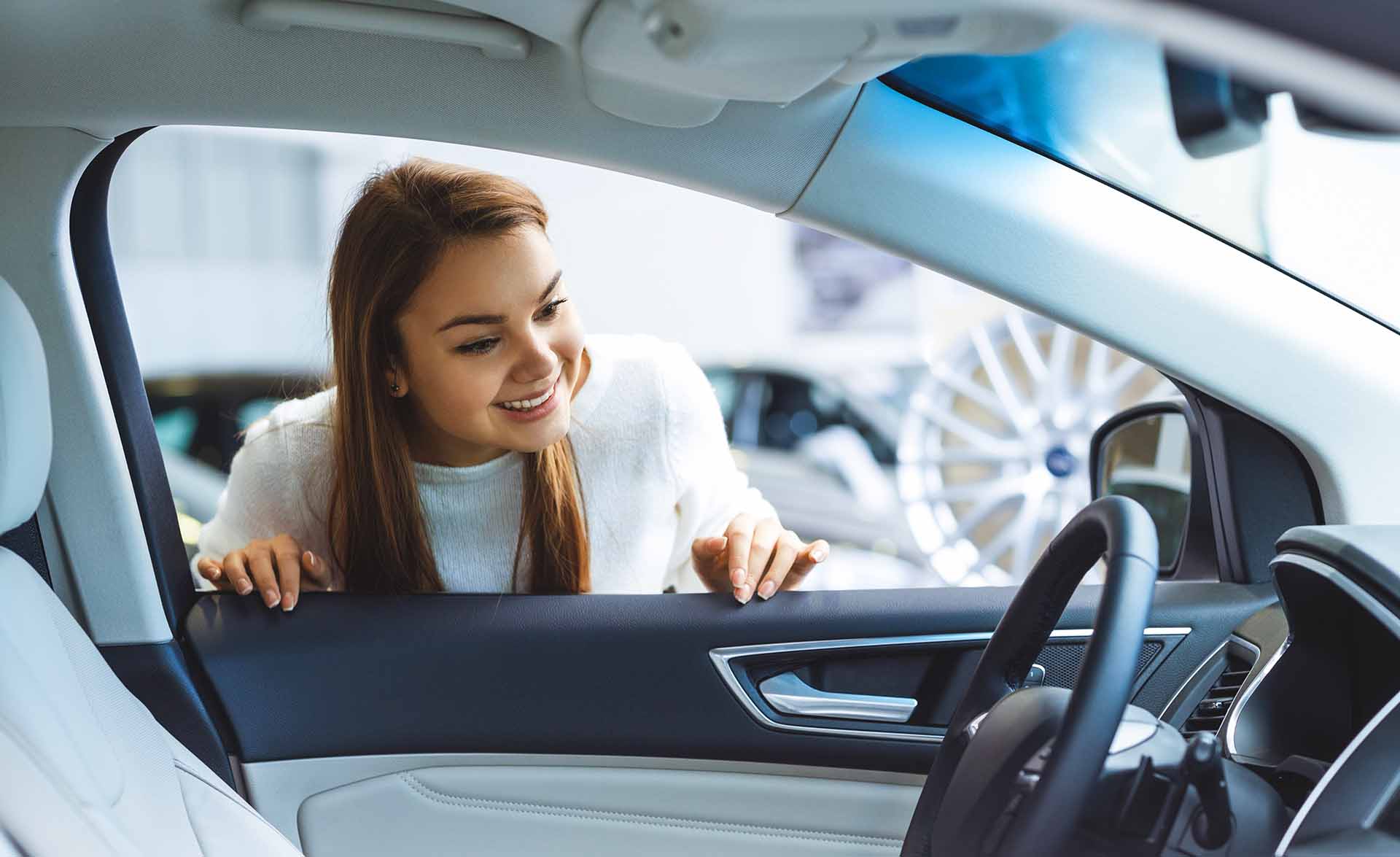 Young woman smiling as she looks into the interior of a vehicle while shopping at a car dealership