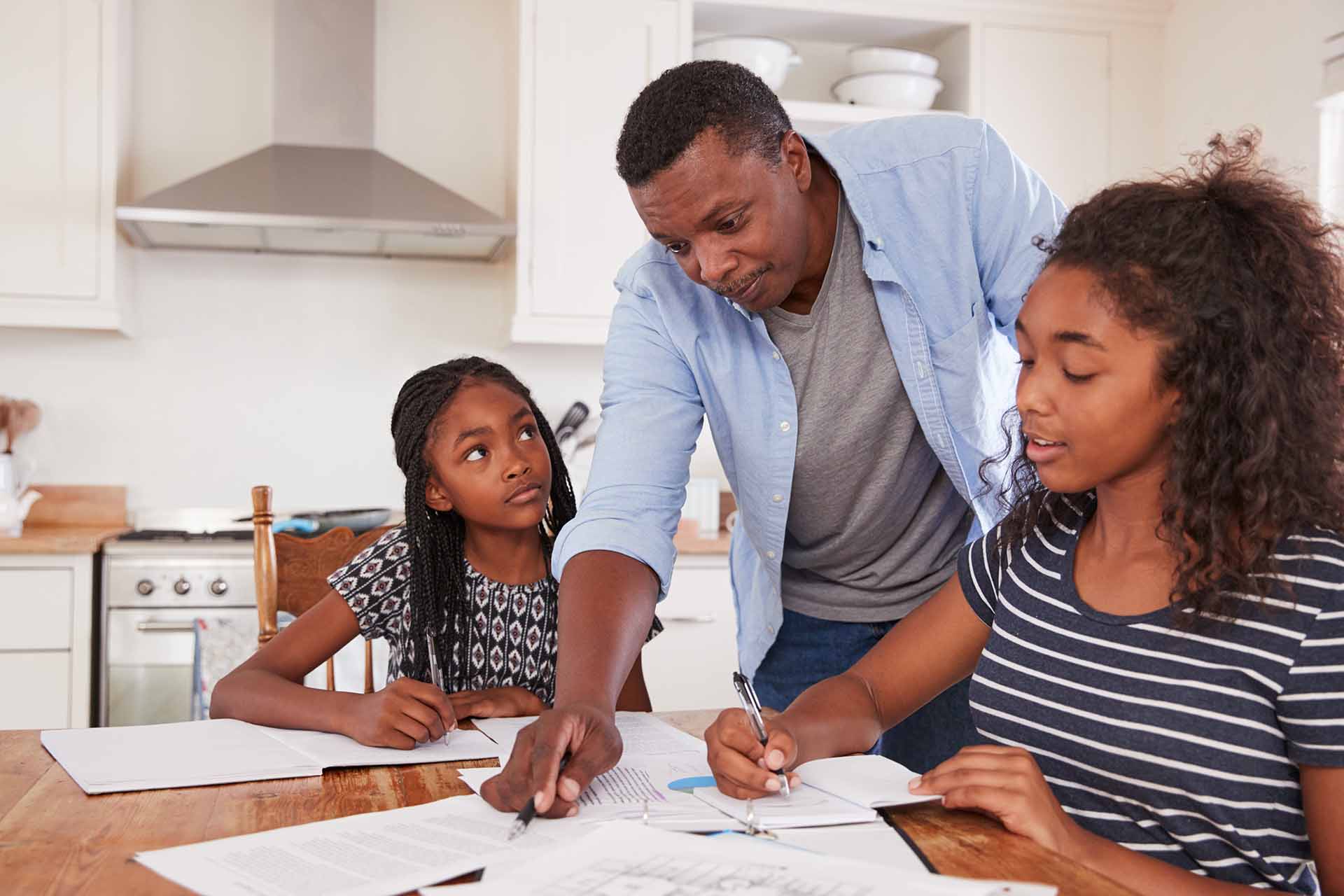 African American father helping teen daughters with homework at the dinner table