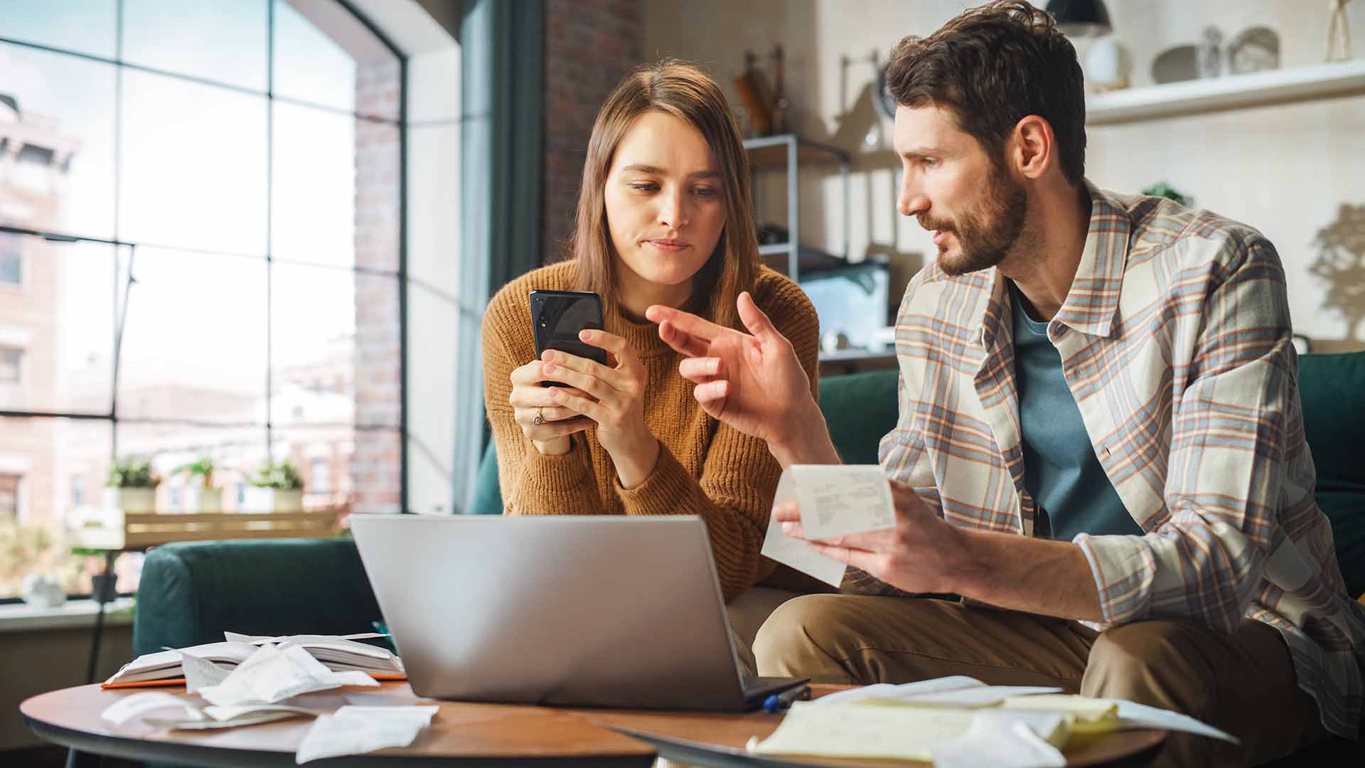 Couple reviewing finances together with receipts, laptop and cell phone at home