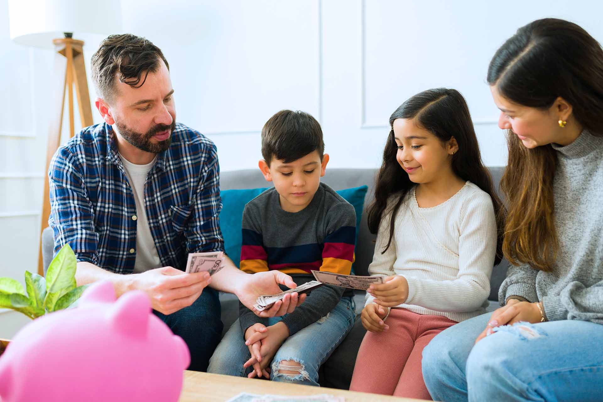Parents sitting on couch with young children and handing them their allowance