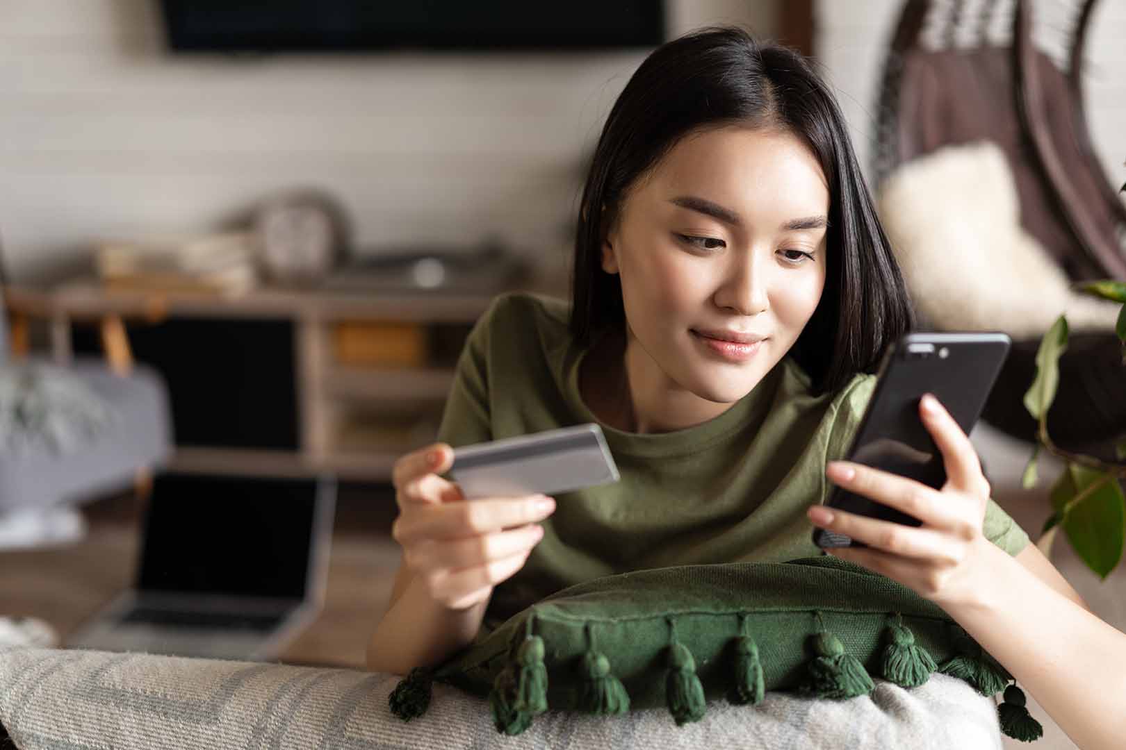 Young Asian woman making purchase on iPhone using credit card from home