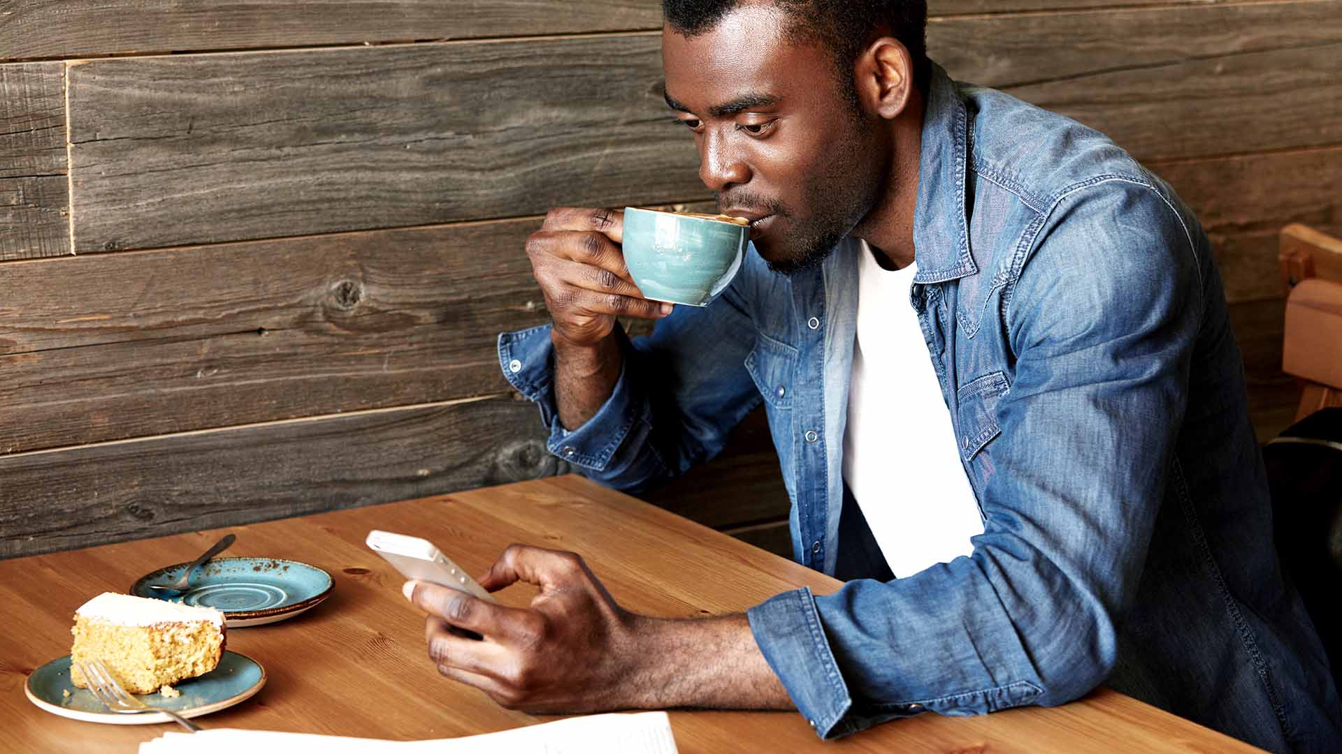 Man drinking coffee in a cafe looking at mobile phone