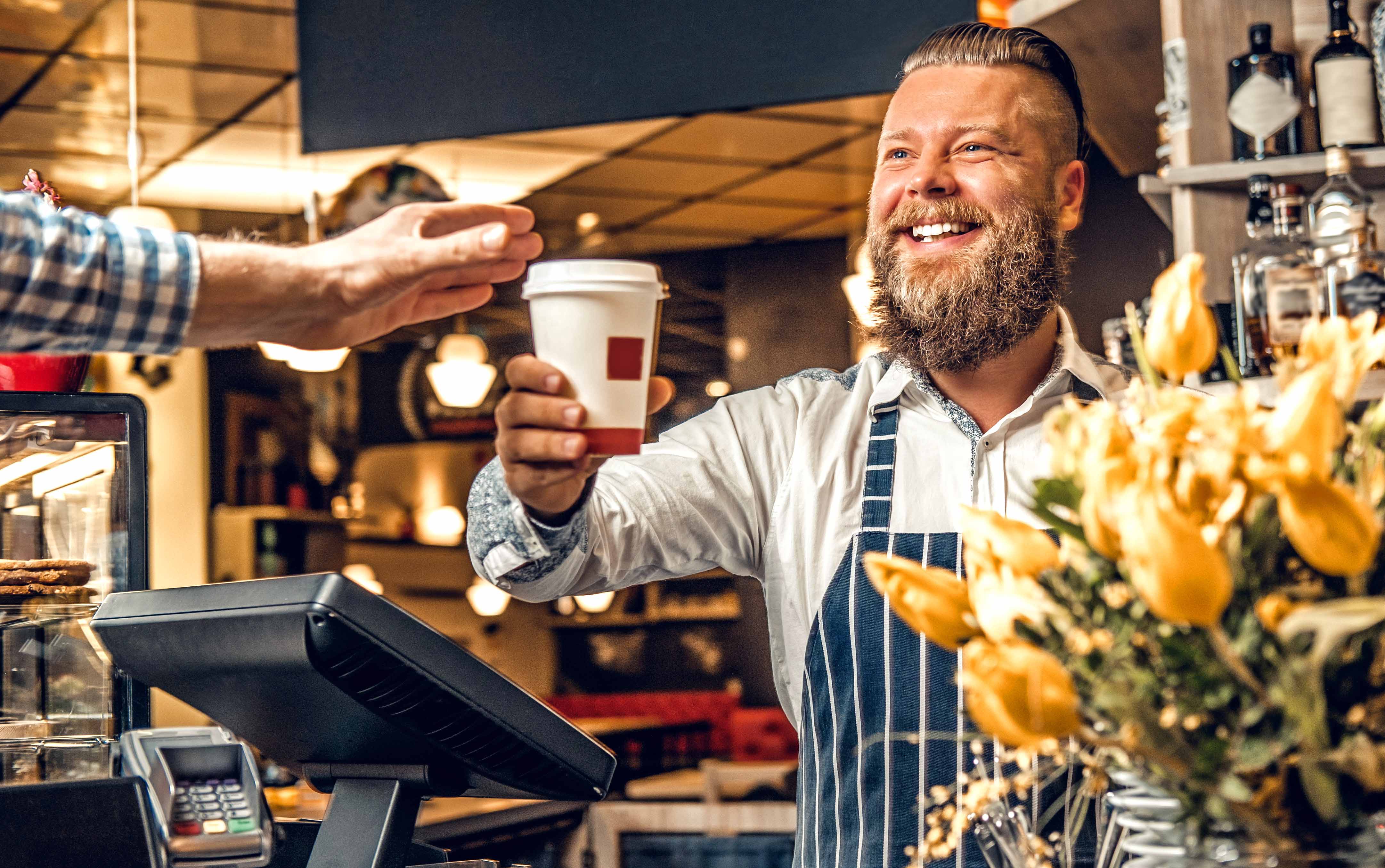 Coffee shop barista handing coffee to customer smiling